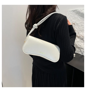 Detalle de bolso de hombro blanco brillante con nudo y letras doradas sobre una modelo