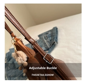 Detail of brown leather tote bag strap with silver metal buckle and soft plush ball charm