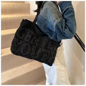 Detail of black denim tote bag with frayed Gentle Youth embroidery on a model