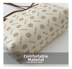 Close-up of beige tote bag floral monogram pattern and brown leather handle stitching