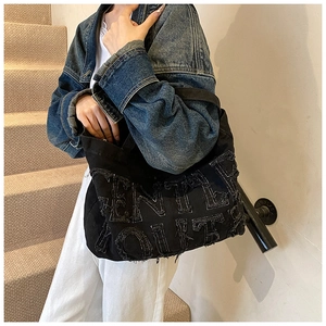 Detail shot of black denim tote bag with frayed GENTLY LOVETT lettering on shoulder