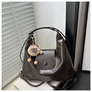 Close-up of deep brown leather tote with crescent design and lion plush pendant