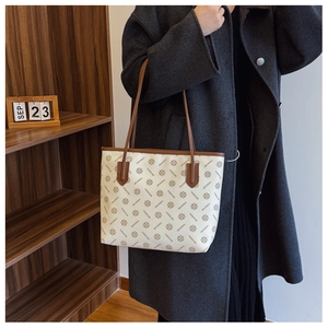 Detail of a large tote bag featuring vintage brown logo print and slim leather straps