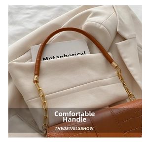 Detail of crocodile pattern handbag with gold chain strap on white blazer