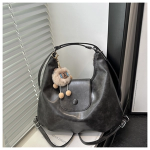 Detail of matte black retro tote bag with brown plush pendant and magnetic flap closure