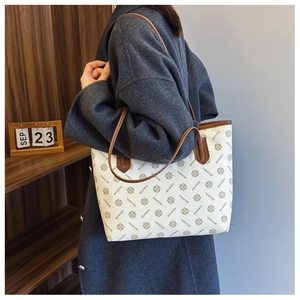 Detail of printed tote bag with brown leather handles and monogram flower pattern