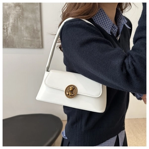 Close-up of white leather underarm bag featuring a vintage golden bear metal buckle