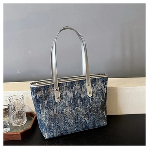Detailed close-up of blue and grey tweed tote bag with silver handles on a modern white desk