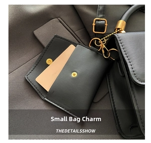 Close-up of black leather mini charm bag with gold snap button and metal chain link