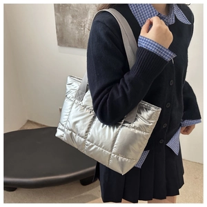 Detailed view of silver quilted puffer tote bag on shoulder with gray strap