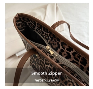 Close-up of golden metal zipper and brown leather trim on leopard print tote bag
