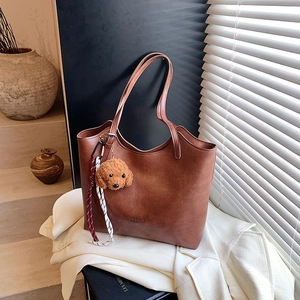 Brown leather tote bag with teddy charm in minimalist studio lighting for autumn style