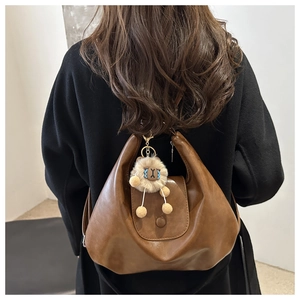 Detail of a brown leather crescent tote bag featuring a cute plush sheep charm on a coat