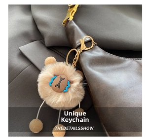 Close-up of a plush light brown bag charm with gold metal buckle on a leather tote