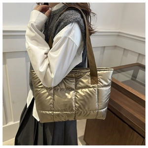 Close-up of metallic quilted puff tote bag with gold finish and woven shoulder strap