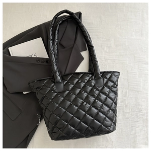 Detailed top view of a black quilted puffer tote bag on a textured grey blazer