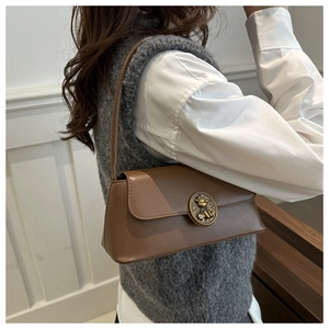 Detail of vintage brown leather underarm bag featuring a round metal bear relief buckle