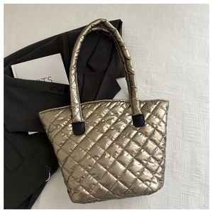 Detail of gold quilted tote bag featuring metallic texture and black leather handle accents