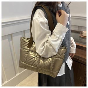 Detail of golden quilted padded tote bag featuring shiny metallic finish and woven strap