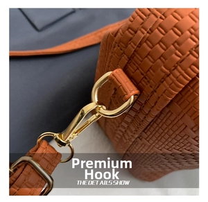 Nahaufnahme des goldenen Karabinerverschlusses an einer braun gewebten Handtasche