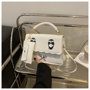 Detailed view of white skull print handbag with hanging mini pouch and metal hardware