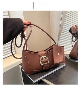 Detail of brown leather underarm bag featuring a vintage horseshoe buckle and a small pouch