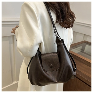 Detail view of large dark brown leather tote bag with flap cover on a white blazer