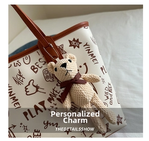 Close-up of a cute plush bear charm with a brown bow on a graffiti tote bag