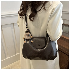 Detail of dark brown leather crescent bag featuring a magnetic flap and plush bear charm