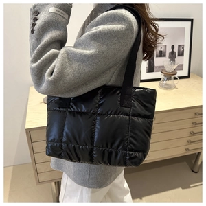 Detailed close-up of a black quilted tote bag worn over the shoulder in a cozy studio setting