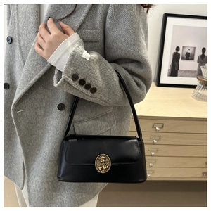 Detail of a black leather rectangular underarm bag with a golden embossed metal buckle