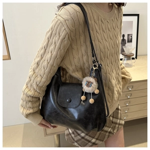 Close-up of black retro hobo bag in glossy PU leather with a cute lion plush pendant