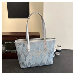 Detail view of light blue sequined denim tote bag with wavy patterns in a cafe setting