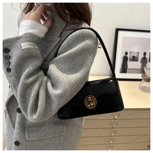 Close-up of retro black leather shoulder bag with a gold embossed bear buckle on a model
