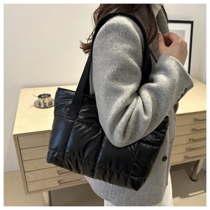 Close-up of a black quilted tote bag with wide strap worn by a model in a warm room