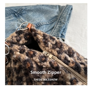 Close-up of smooth metal zipper and brown leather trim on leopard plush tote bag