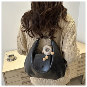 Detailed view of a black crescent shoulder bag with a cute plush pendant on a knit sweater