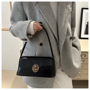 Detail of a black leather shoulder bag featuring a vintage golden bear buckle on the flap