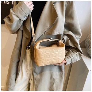 Detail einer beige texturierten Umhängetasche mit Goldverschluss am Trenchcoat