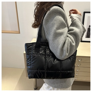 Detail of black quilted puffer tote bag worn by a model in a grey herringbone blazer