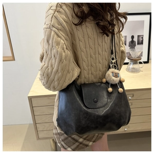 Detail of vintage black leather crossbody bag featuring a plush sheep charm accessory