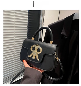Detail der schwarzen Handtasche aus Leder mit goldenem R-Metallverschluss und Griff