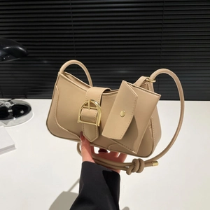 Beige crescent underarm bag with gold buckle and mini pouch accessory in hand