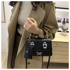 Detail view of black skull print handbag featuring a detachable matching coin purse accessory