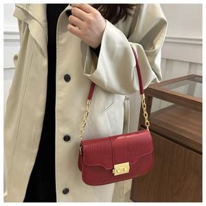 Detail of dark red croc-embossed underarm bag with gold metal buckle on a beige trench coat