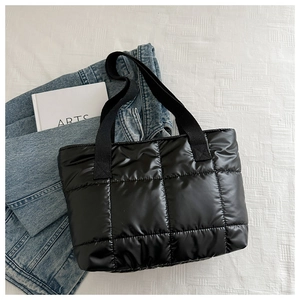 Detailed view of black quilted puffer tote bag with glossy finish on a textured background