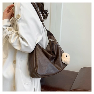 Deep brown faux leather hobo bag with plush charm shown on a white winter coat