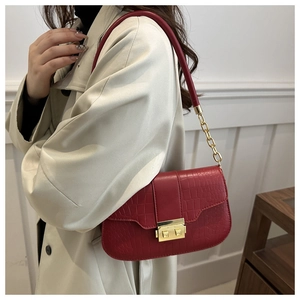 Detail of red crocodile pattern handbag featuring a gold metal buckle and chain strap
