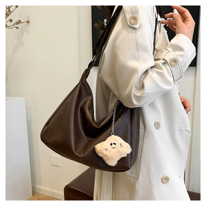 Macro detail of dark brown pebble leather hobo bag with cute plush smiley charm