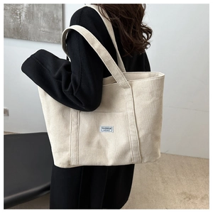 Detail of off-white corduroy tote bag showing textured fabric and fashion label